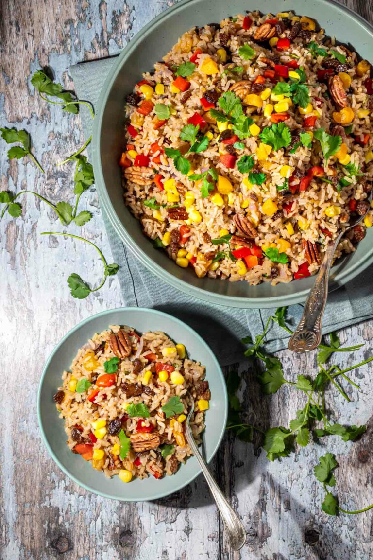Two bowls of brown rice salad with serving spoons.