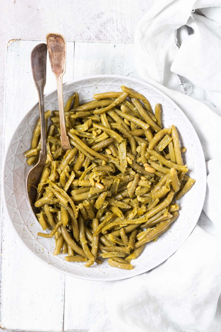 top down view of the completed how to cook canned green beans recipe in a white dish with serving spoons
