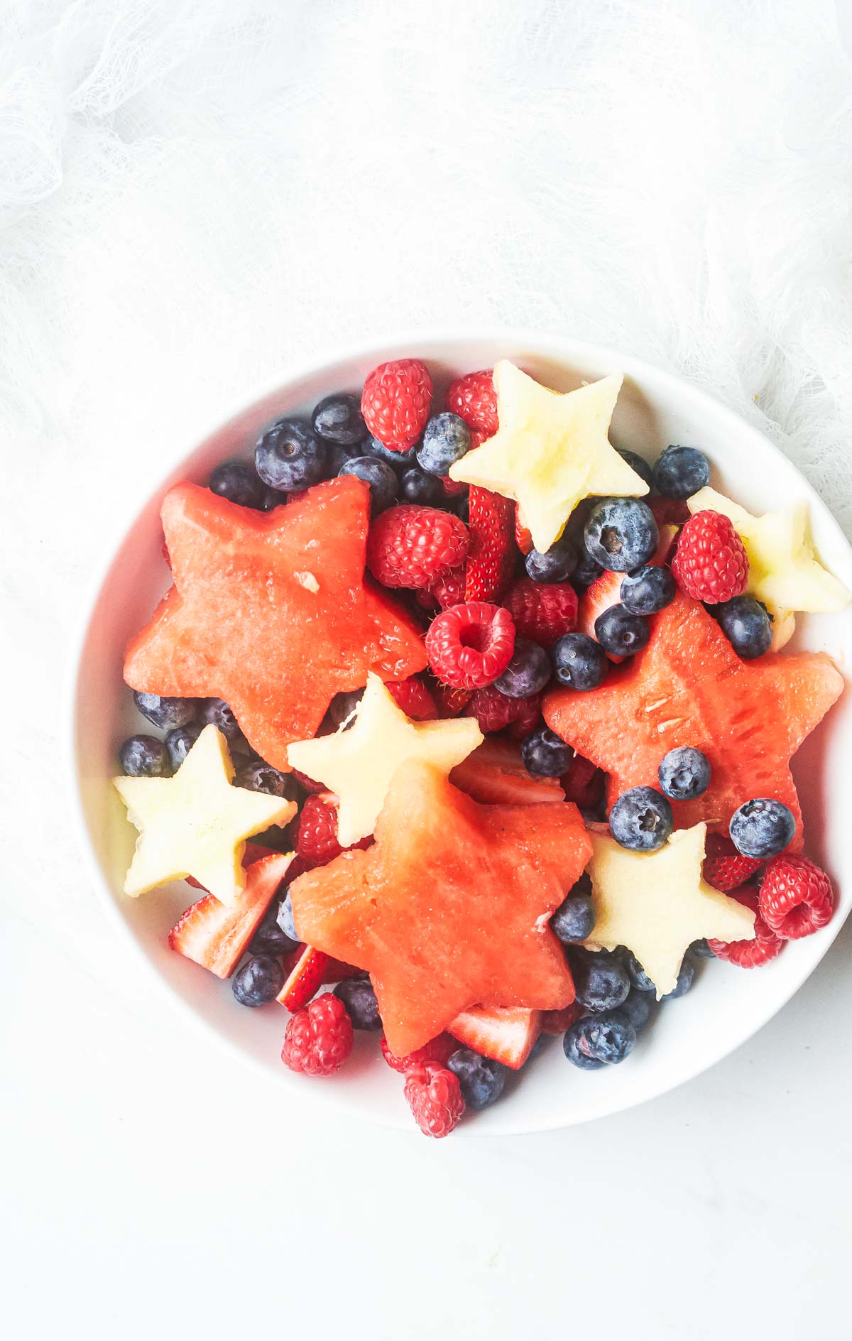 a plate of patriotic fruit salad, with berries, apple and melon in a bowl on a table