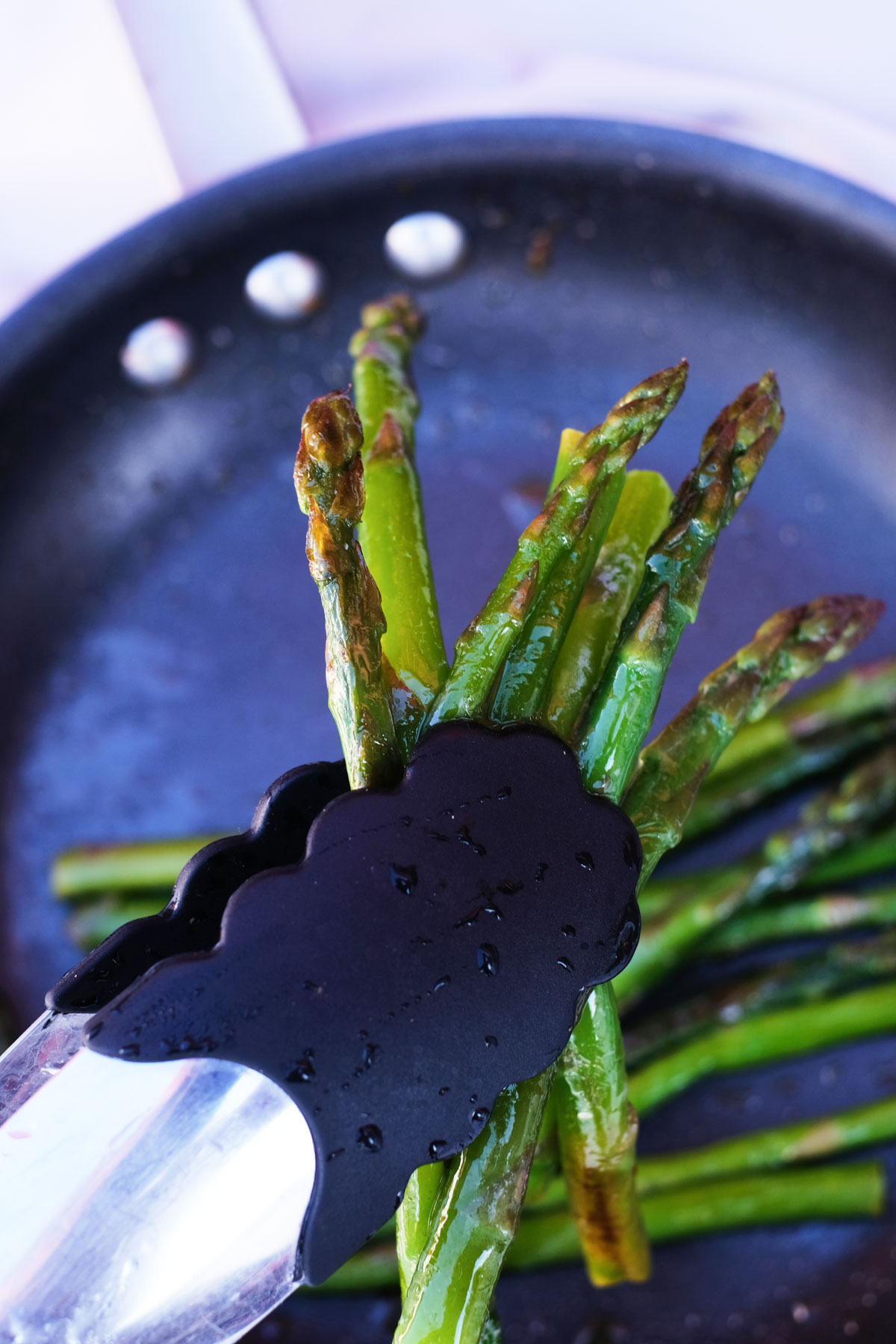 close up view of tongs removing cooked frozen asparagus from a skillet