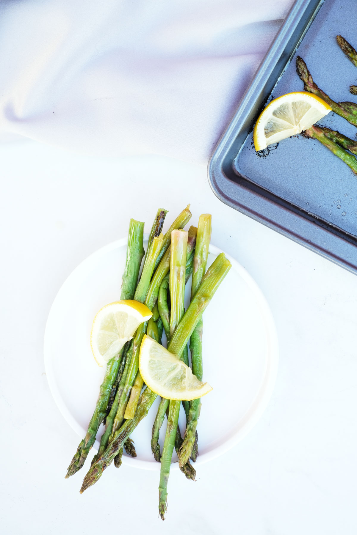 top down view of cooked frozen asparagus on a white plate next to a sheet pan