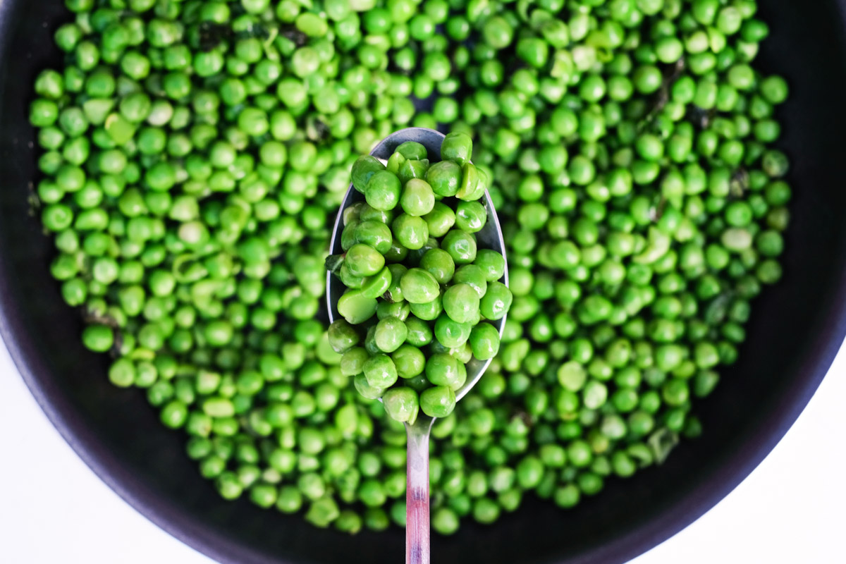 close up view of a spoon removing cooked frozen peas from a pan