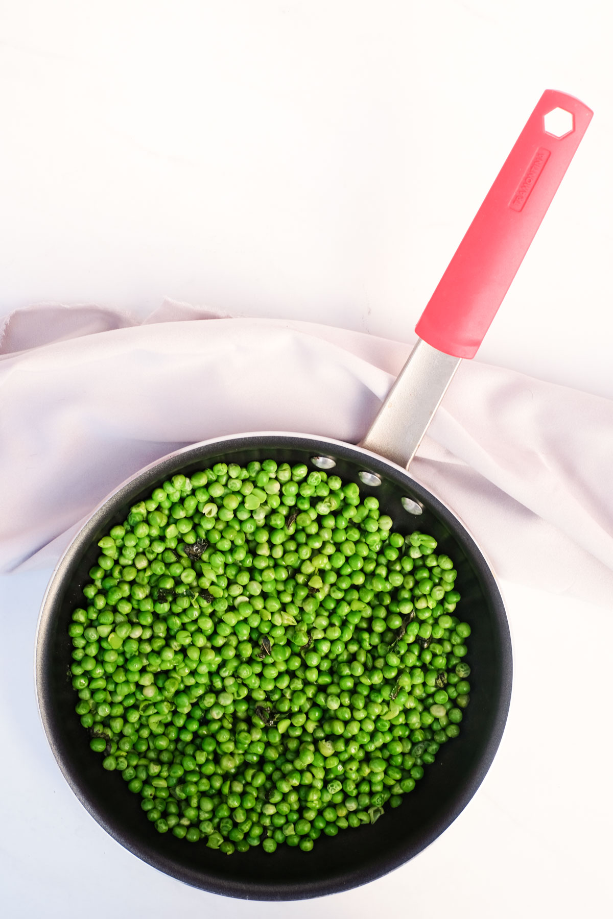 top down view of how to cook frozen peas in a skillet with a read handle