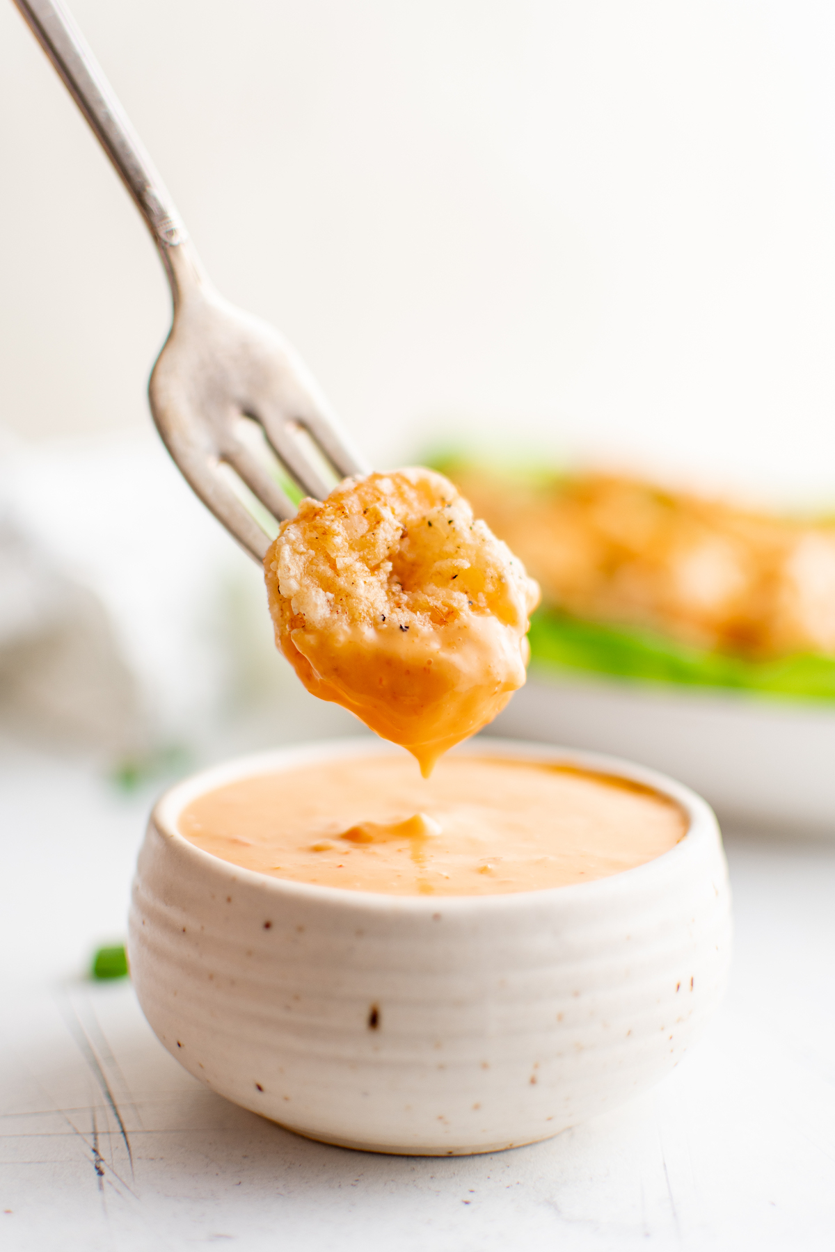 one piece of bang bang shrimp on a fork being dipped into sauce