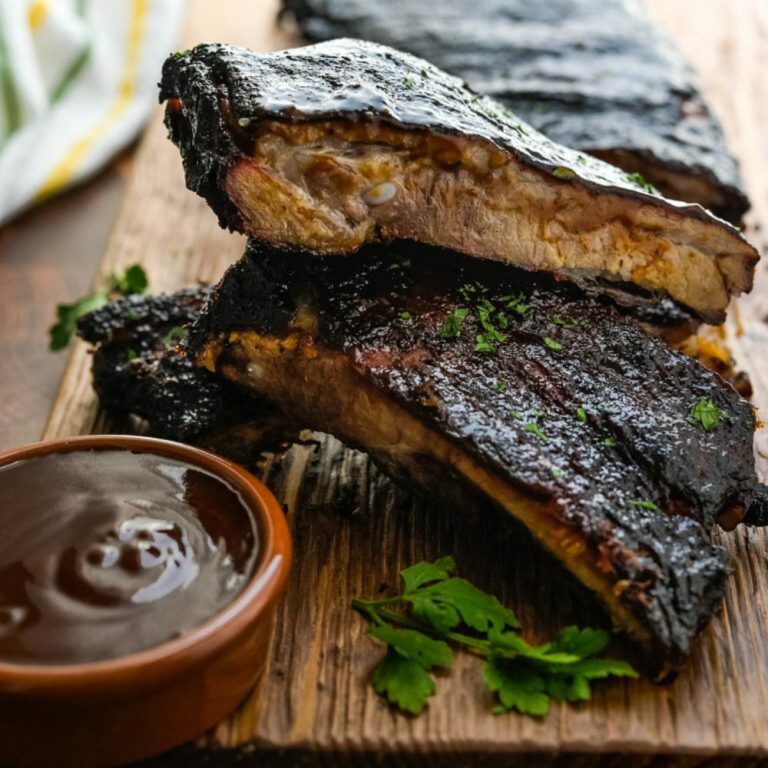 Kansas City Smoked Spareribs on a wooden chopping board with barbeque sauce.