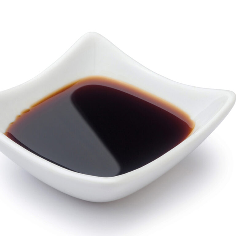 A small square ceramic dish full of soy sauce.