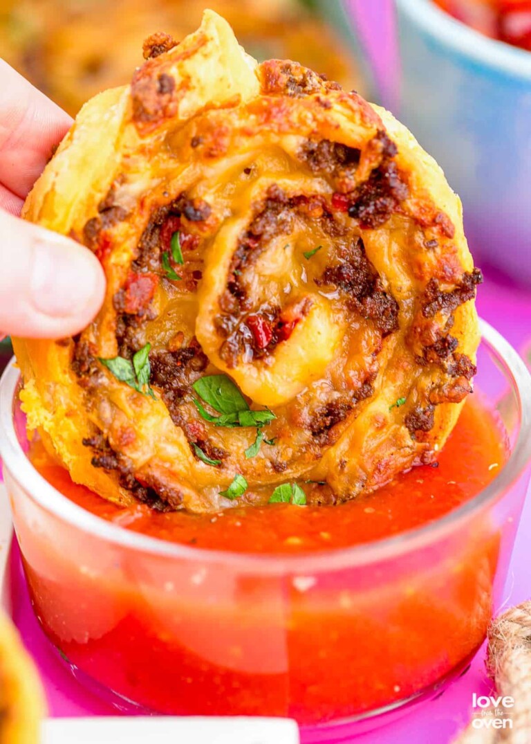 a close up of one of the taco pinwheels being dipped into a cup of salsa