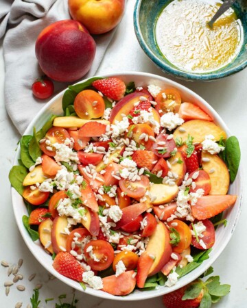 the tomato feta salad served next to a bowl of honey mustard dressing and two peaches