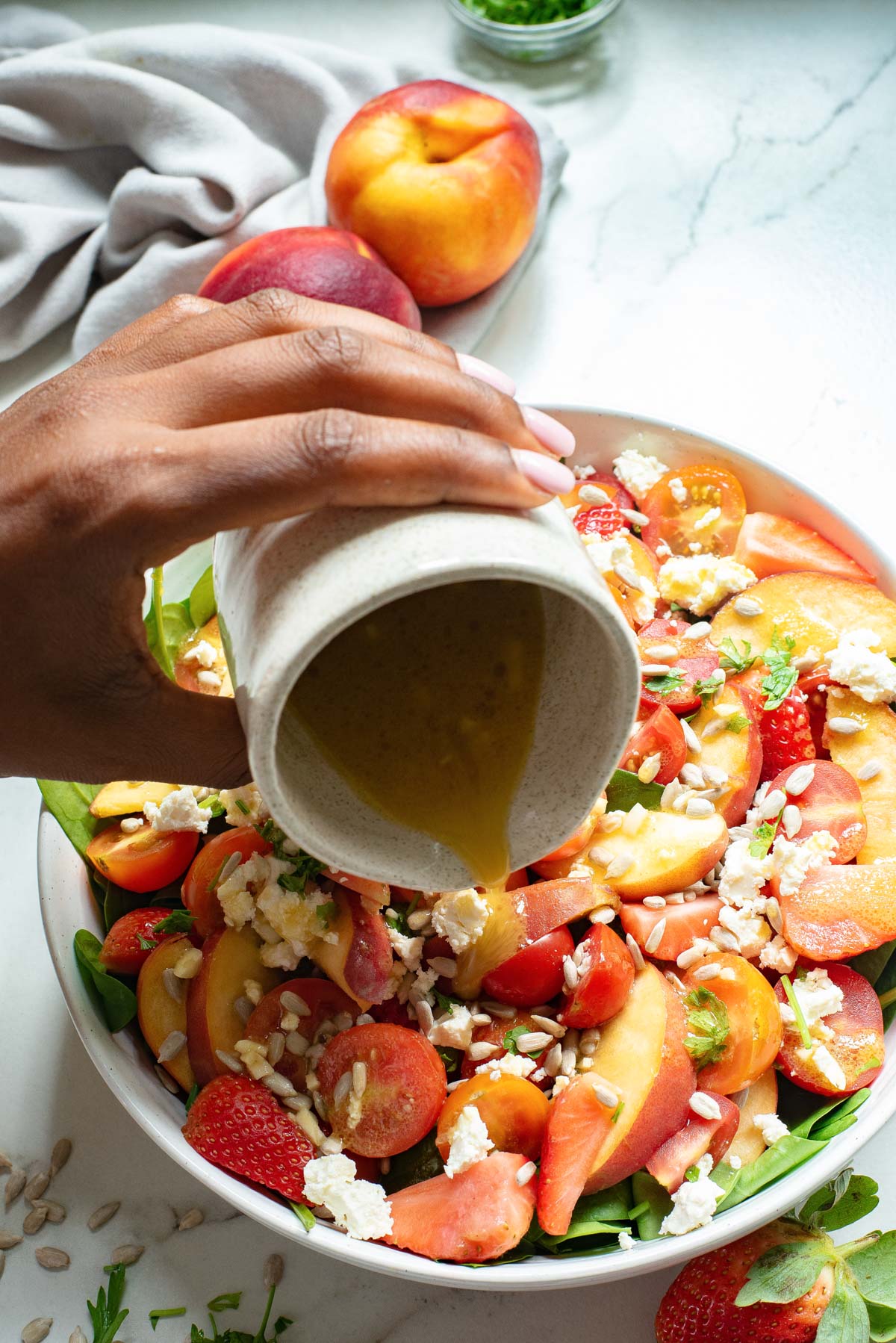 honey mustard dressing being poured over a bowl of tomato feta salad