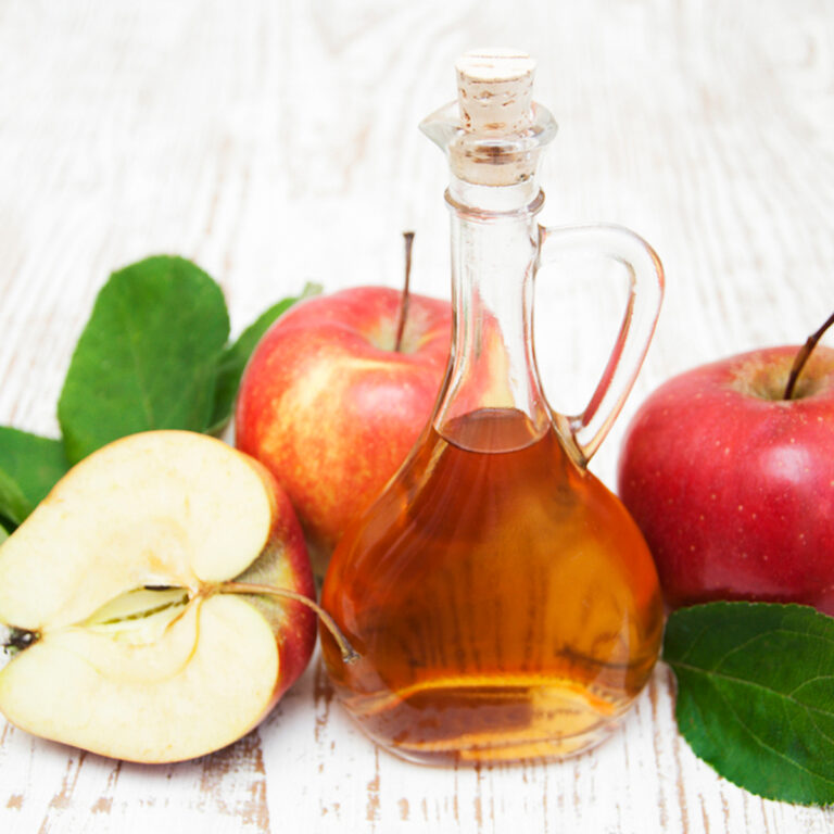 Apple cider vinegar in a glass decanter surrounded by red apples and leaves