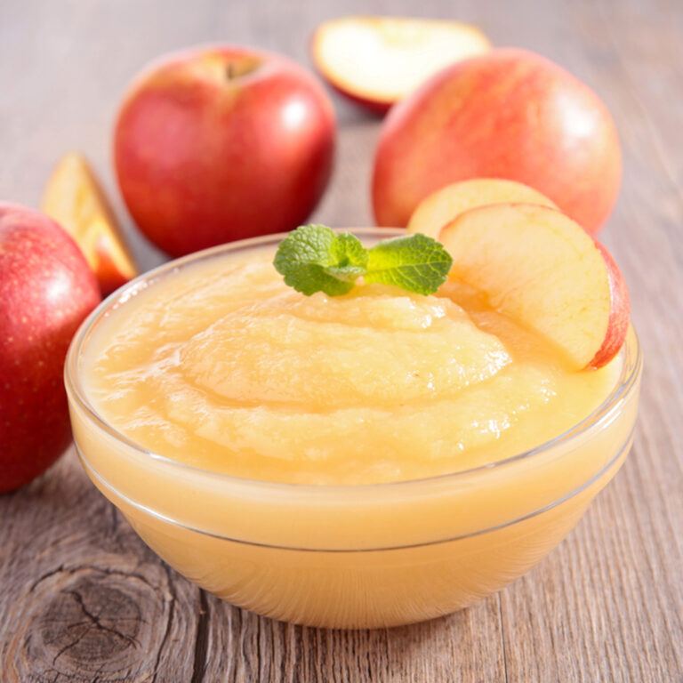 A glass bowl of apple sauce with several apples in the background