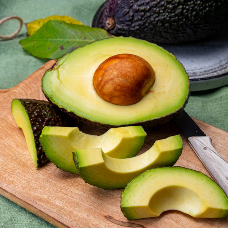 A halved avocado on a cutting board with slices of avocado sitting beside it