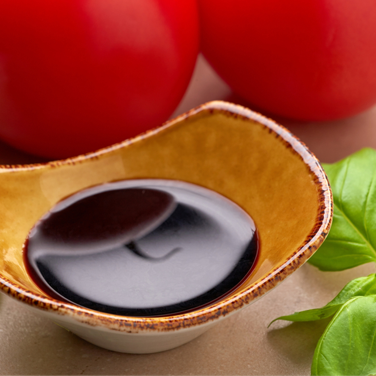 a ceramic dish containing Balsamic glaze set in front of two tomatoes