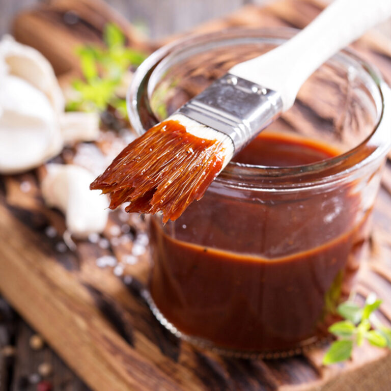 A glass jar of barbecue sauce with a brush sitting on top of it.