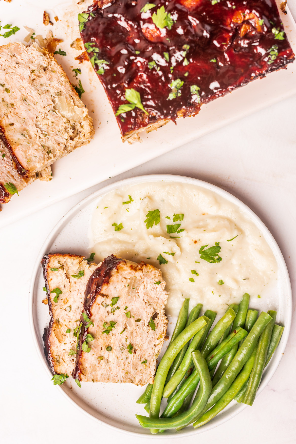 chicken meatloaf served on a dinner plate with green beans and mashed potatoes