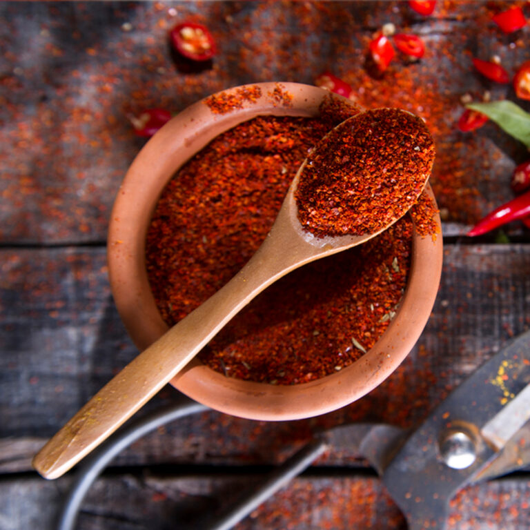 Overhead view of a bowl of chili powder with a spoon sitting on top of it.