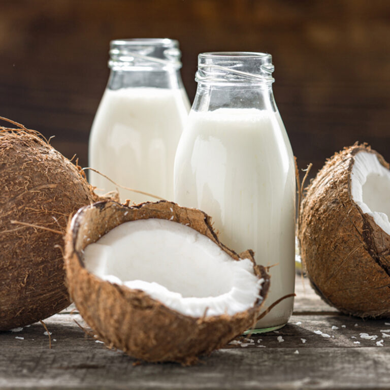 two bottles of coconut milk surrounded by halved coconuts