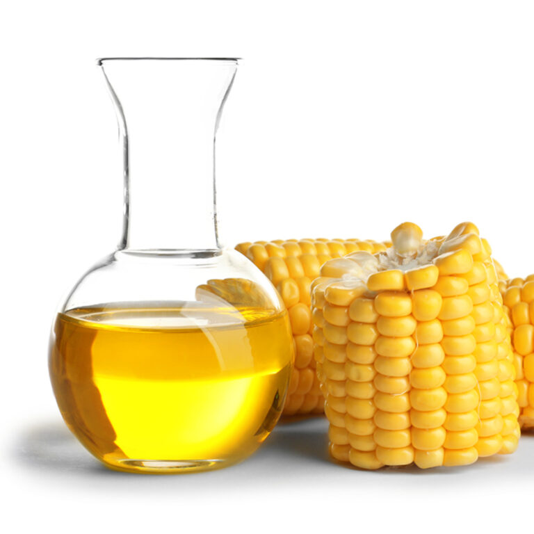 A glass carafe of corn syrup with a sliced fresh corn cob sitting beside it