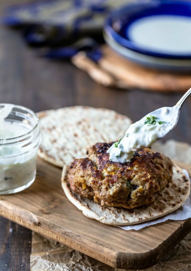 one greek chicken burger being topped with yogurt sauce