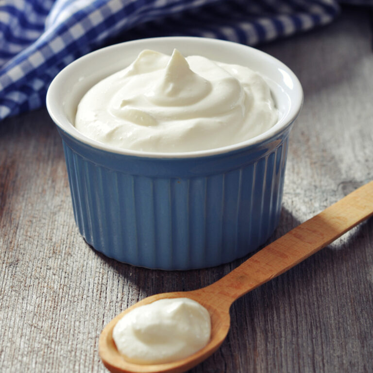 A ceramic dish of greek yogurt with a wooden spoon sitting in front of it