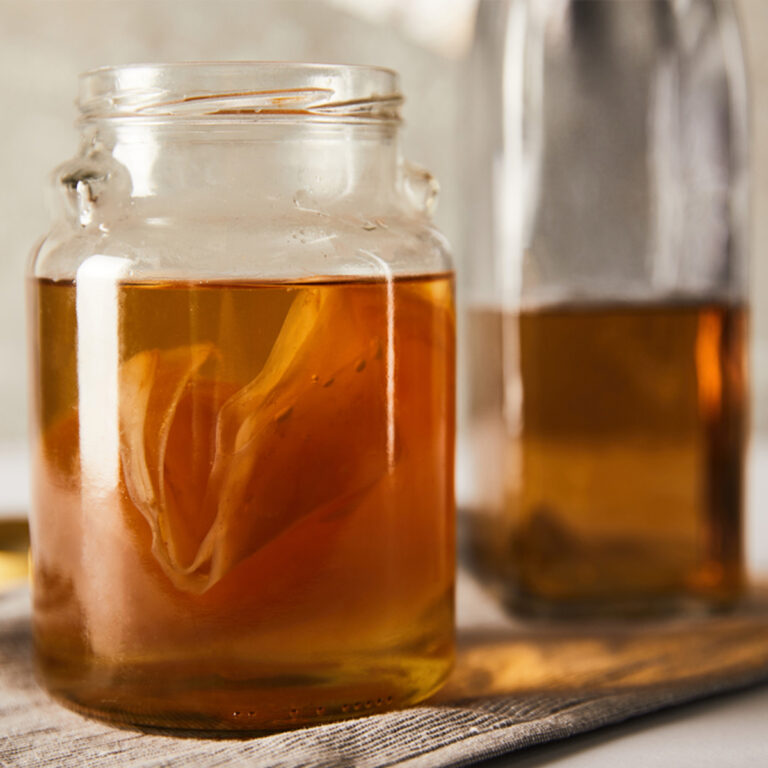 A wide-mouthed jar of kombucha with another bottle in the background