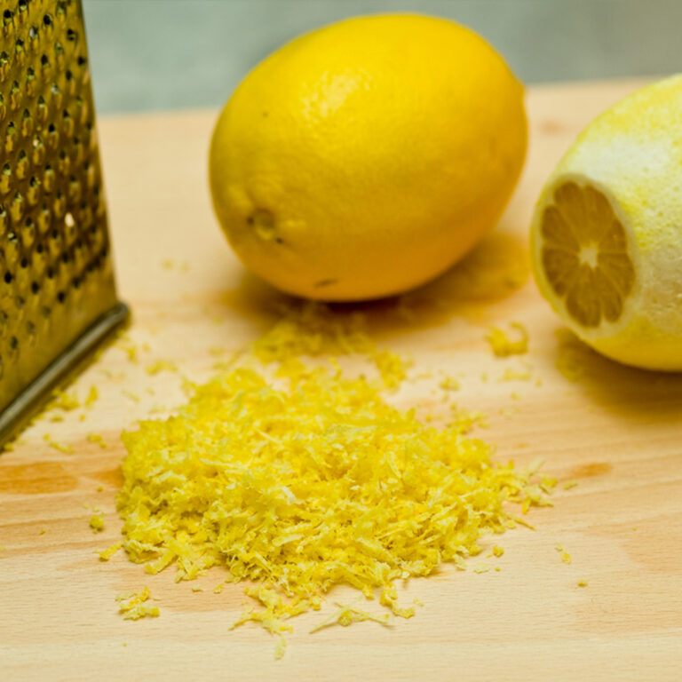 A pile of lemon zest on a countertop with a grater and a whole lemon behind it.