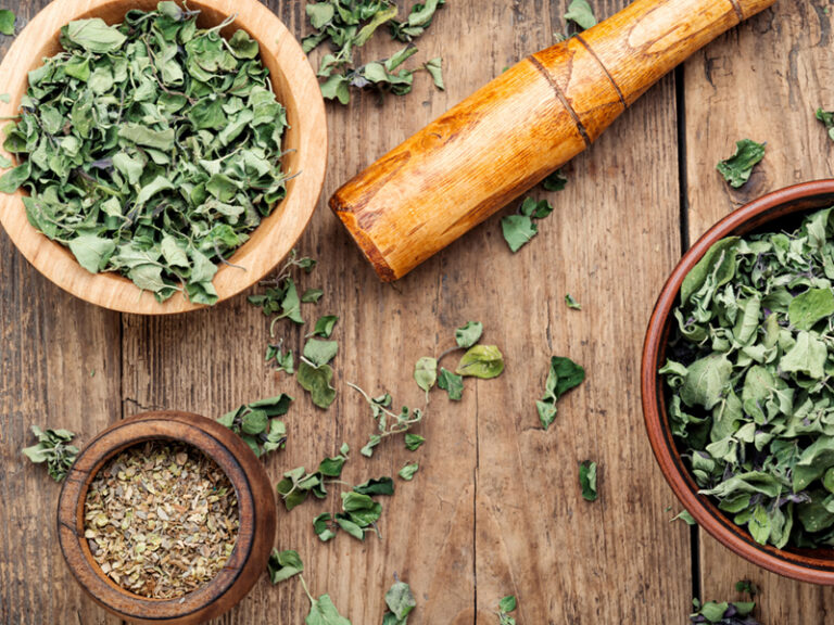 Overhead view of bowls of marjoram with a wooden pestle sitting on a wooden tabletop