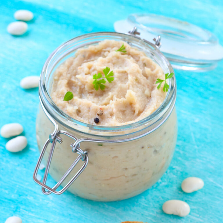 A jar of mashed white bean paste with several whole white beans scattered around it