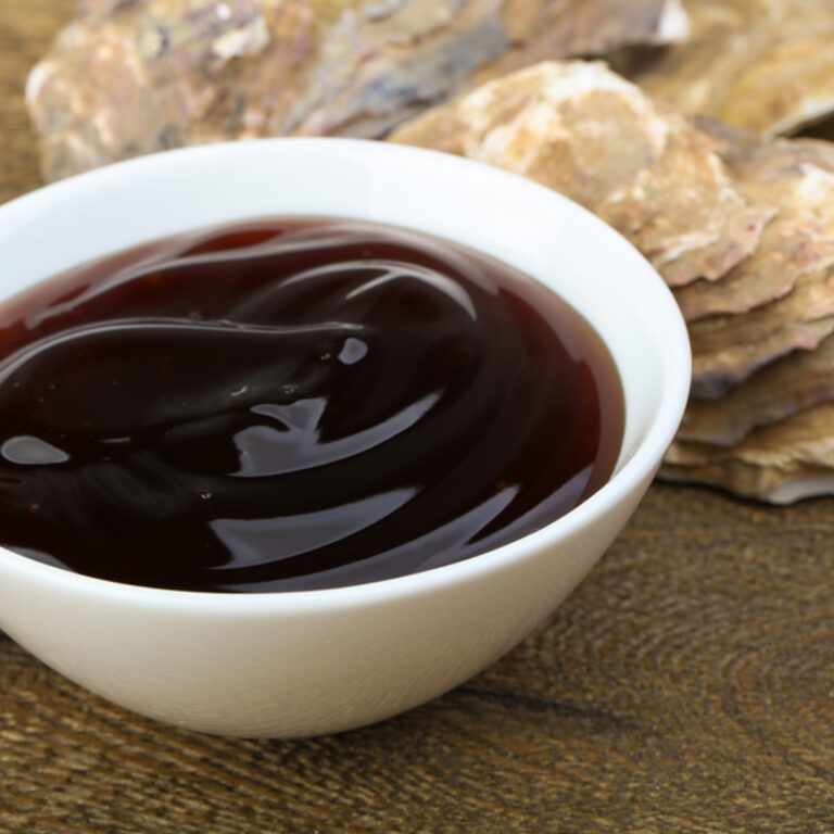 Oyster sauce in a white bowl with oyster shells in the background.