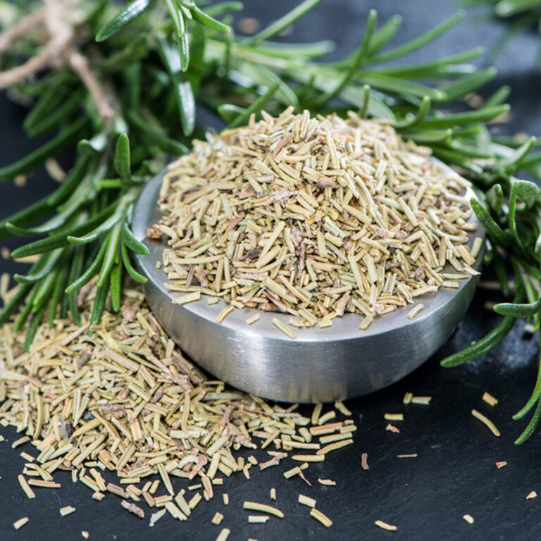 A small metal bowl full of dried rosemary with fresh rosemary sprigs behind it.