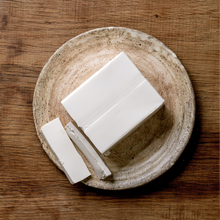 Overhead view of a block of silken tofu with two slices taken out of it sitting on a rustic ceramic plate