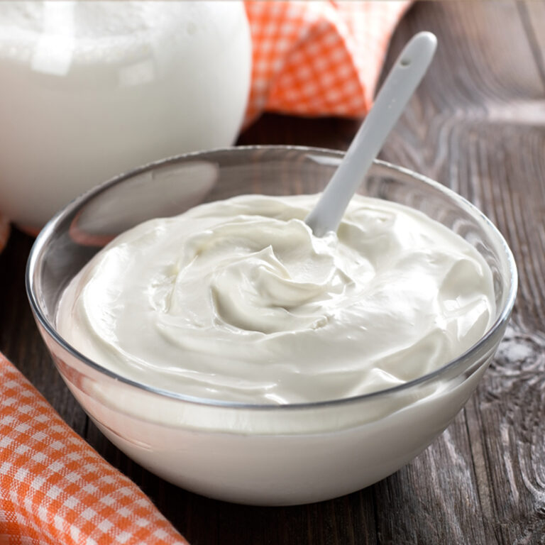 A glass bowl of sour cream with a spoon in it