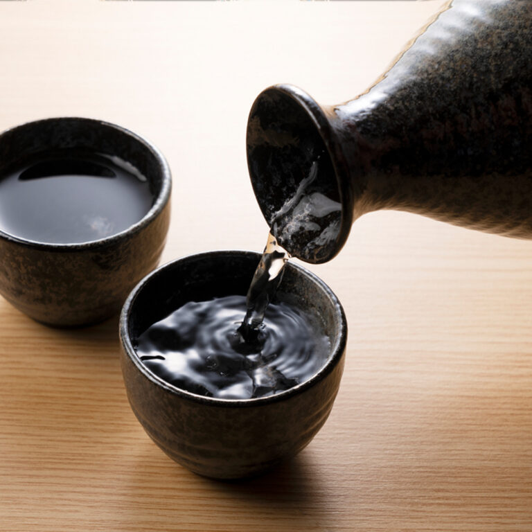 Two small cups with sake being poured into one from a sake bottle