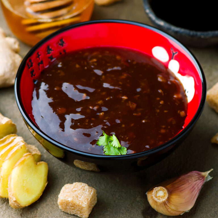 A bowl of teriyaki sauce with ginger and garlic cloves beside it.