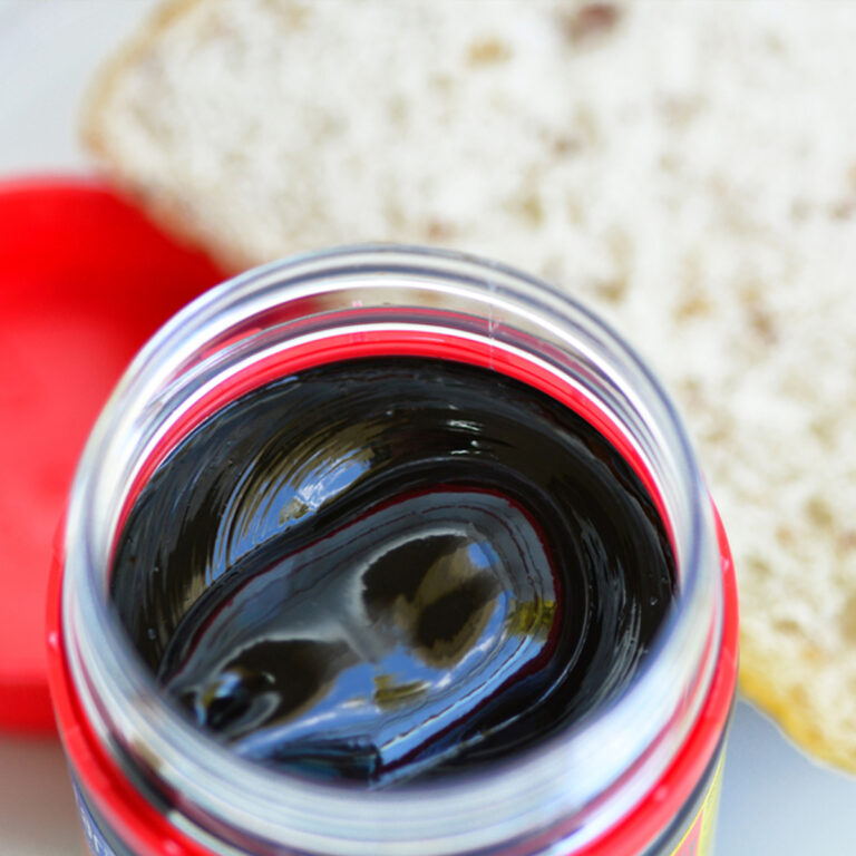 overhead view of an open jar of vegemite next to a slice of bread.