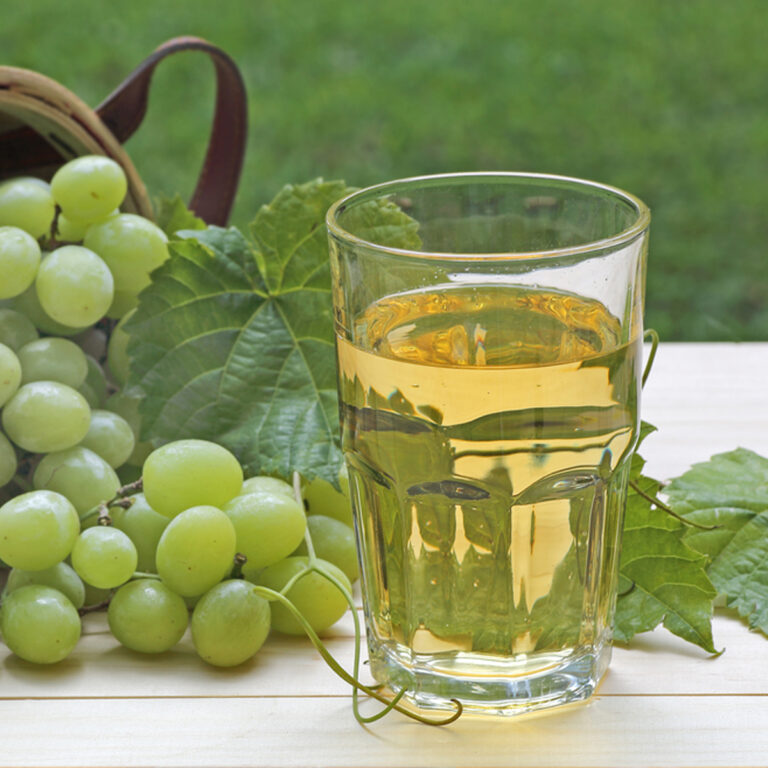 A glass of white grape juice with a bunch of grapes in the background