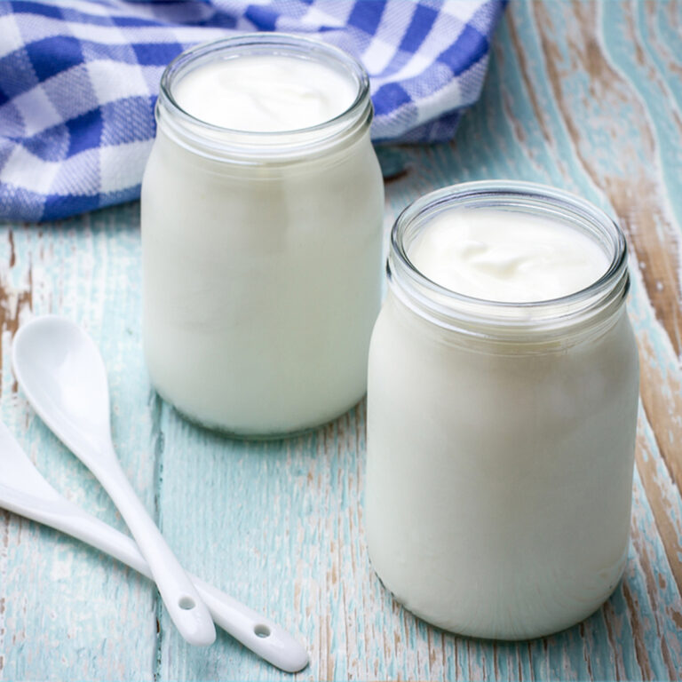 two jars of plain yogurt with two spoons sitting beside them