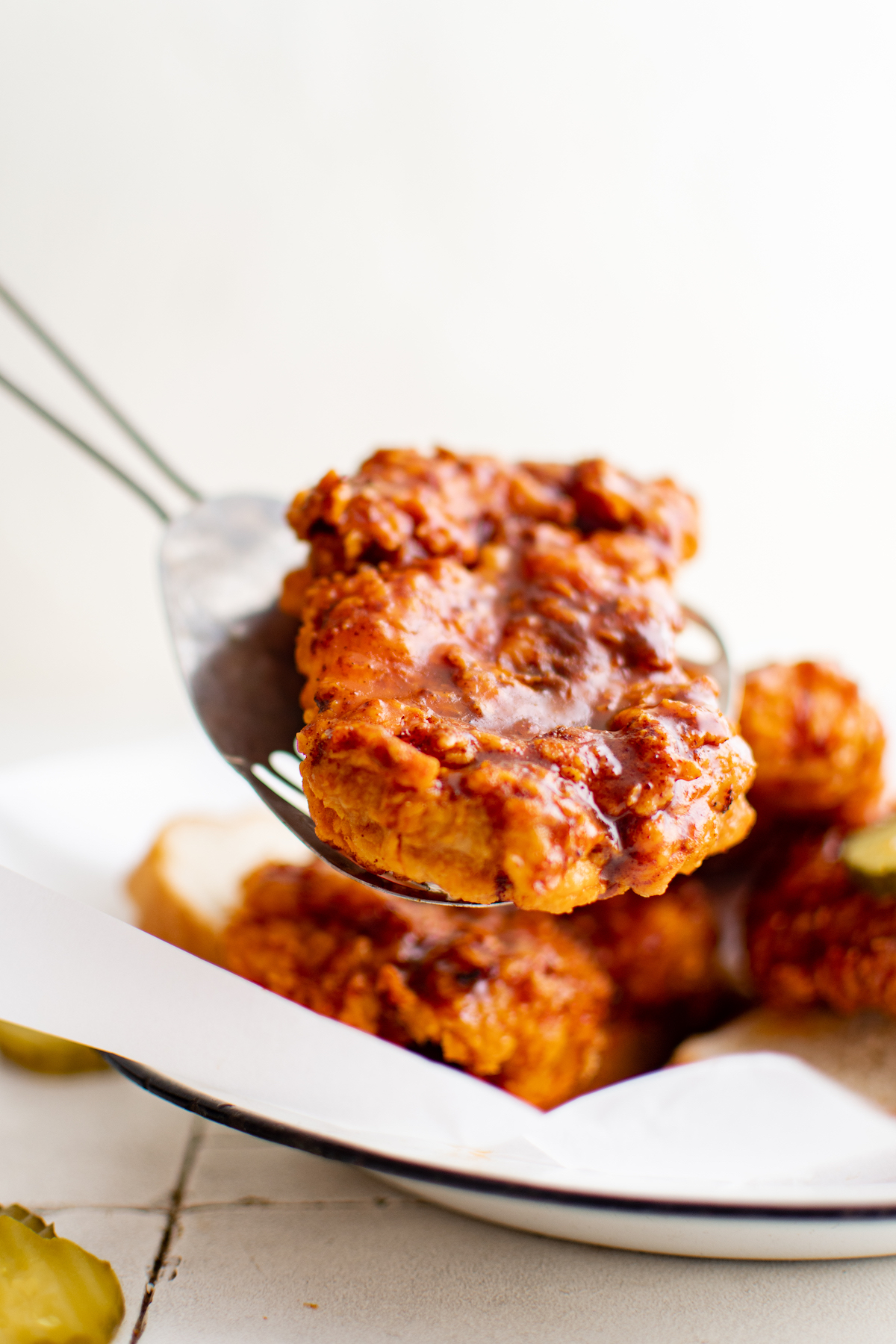 a serving spoon placing a pice of air fryer nashville hot chicken onto a plate