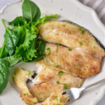 the finished air fryer tilapia on a white plate and garnished with fresh herbs