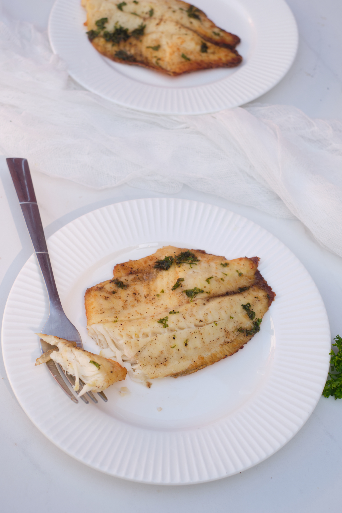 one of the air fryer frozen tilapia filets on a white plate with a fork removing a bite