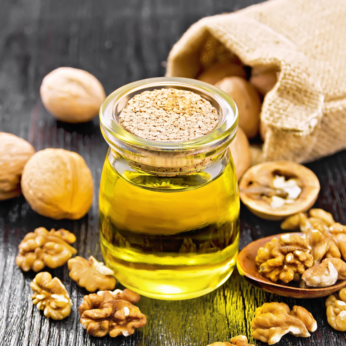 A jar of walnut oil surrounded by shelled walnuts with whole walnuts in the background.