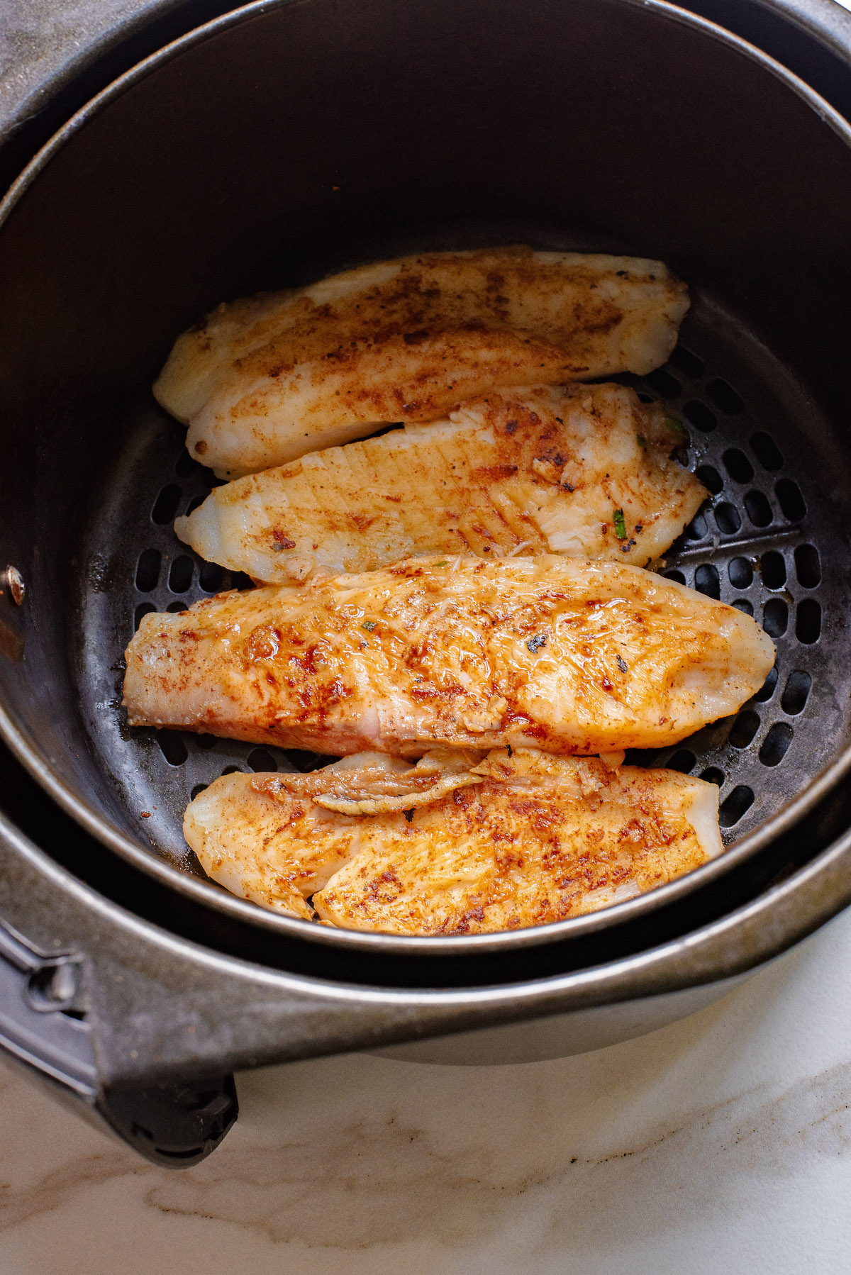 the cooked tilapia fliets for this air fryer fish tacos recipe in the air fryer basket