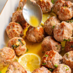 a spoon pouring sauce over the baked turkey meatballs
