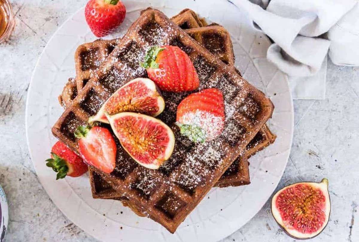 gingerbread waffles stacked on a plate and topped with fruit and powdered sugar