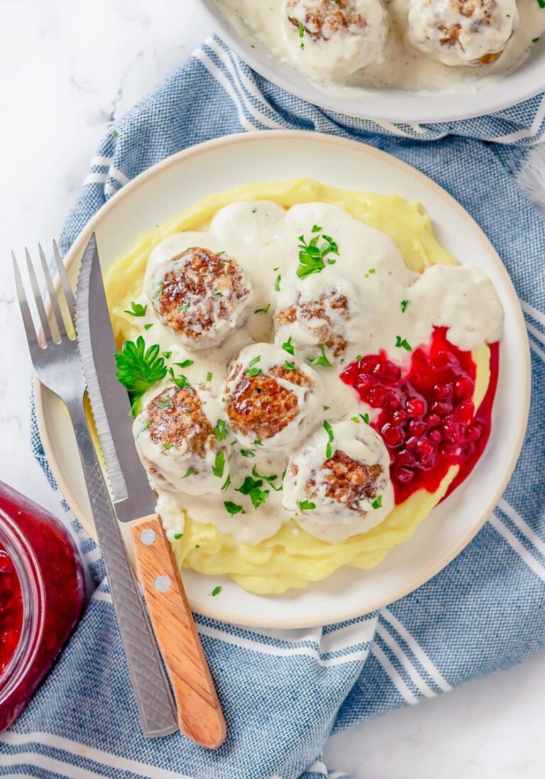 Crockpot swedish meatballs in a white plate with mash and a knife and fork.