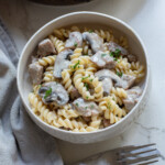 a serving of turkey stroganoff in a white bowl with fork and cloth napkin