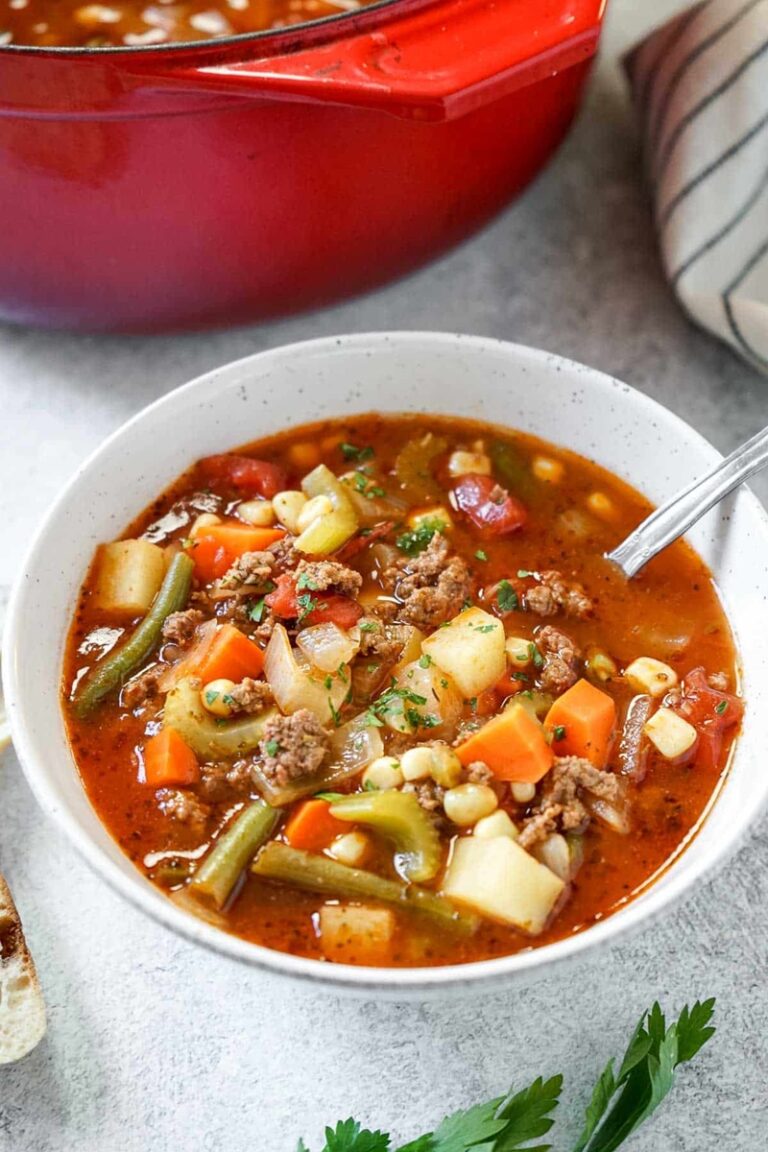 Vegetable beef soup in a white bowl with a spoon.
