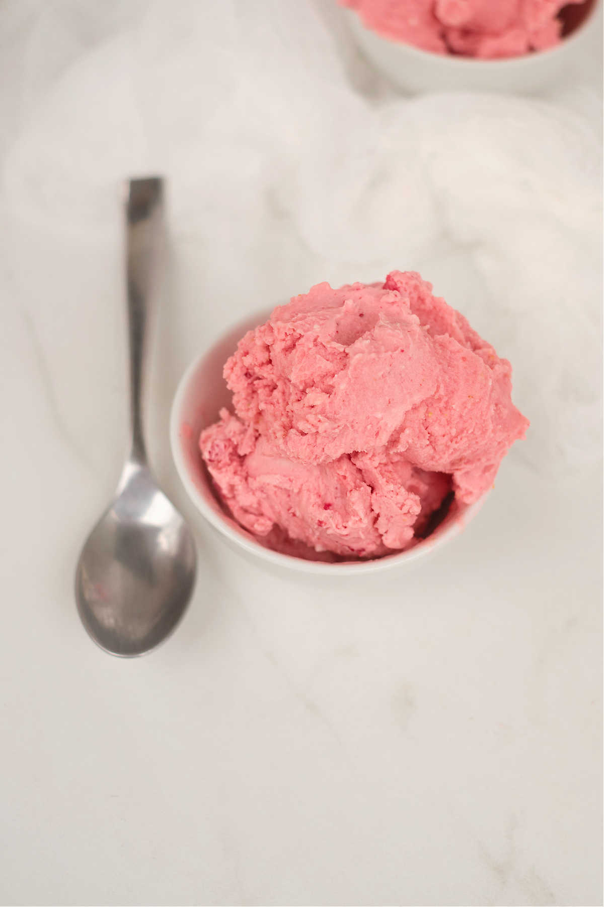 one serving of strawberry flavored ice cream in a bowl next to a spoon