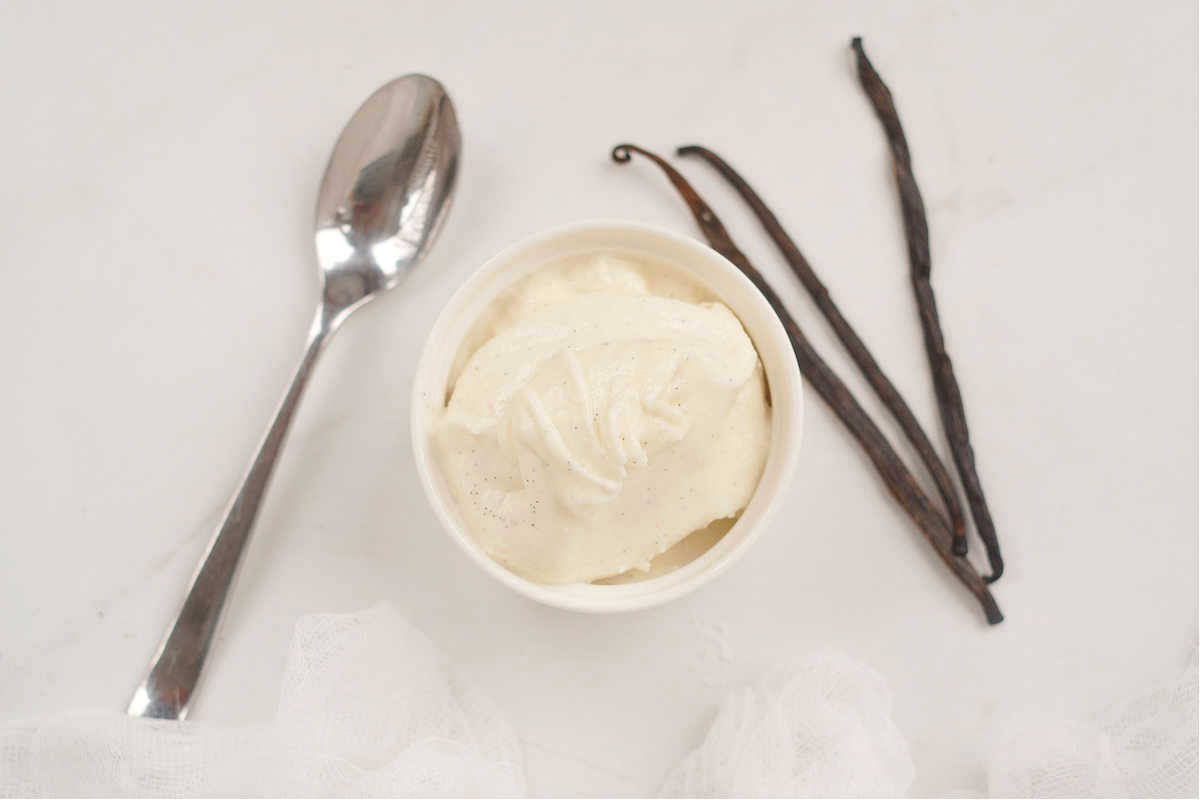 one serving of vanilla ice cream in a ceramic bowl with a spoon on the side