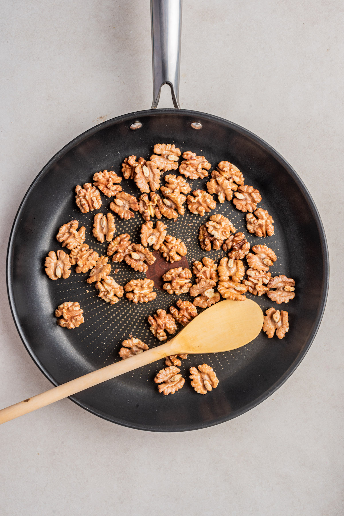 top down view of a wooden spoon stirring walnuts in a skillet